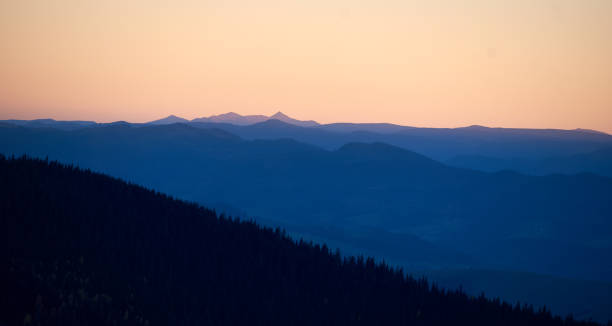 istock Silhouette of distant mountains at sunset, with golden sky transitioning into deep blue shadows. 2205045054