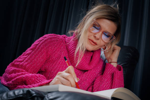 istock Woman wearing fuchsia sweater and glasses writing on a notebook 2205053537
