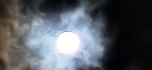 istock The full moon hides behind the clouds, its light dispersed across the cloudy sky. Even partially hidden, the moon gently illuminates the night, creating a contrast of shadows and soft lights. 2205059419