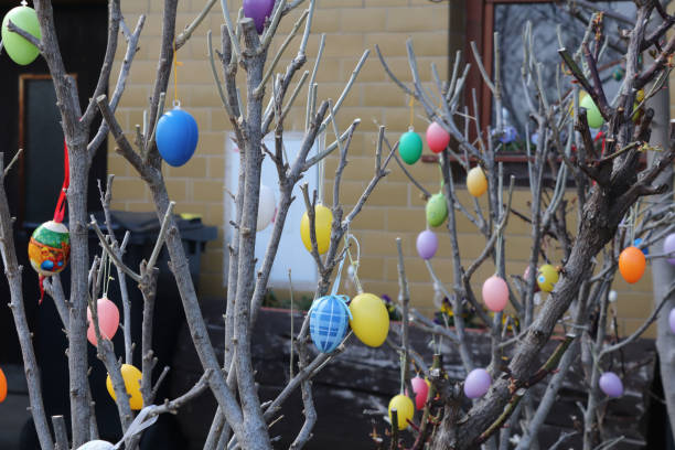 A decorated tree is adorned with colorful Easter eggs, set against a beautiful bright blue sky filled with fluffy white clouds.