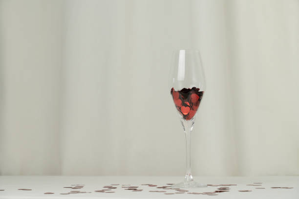 Wine glass with heart confetti on cream background. Minimalist holiday photo for Valentines