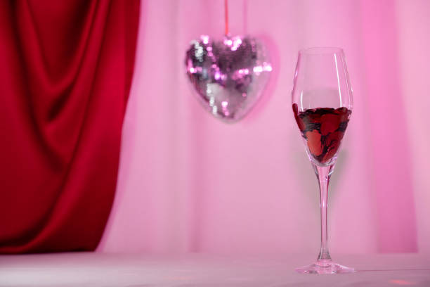 Wine glass with heart confetti and disco on pink background. Minimalist holiday photo for Valentines