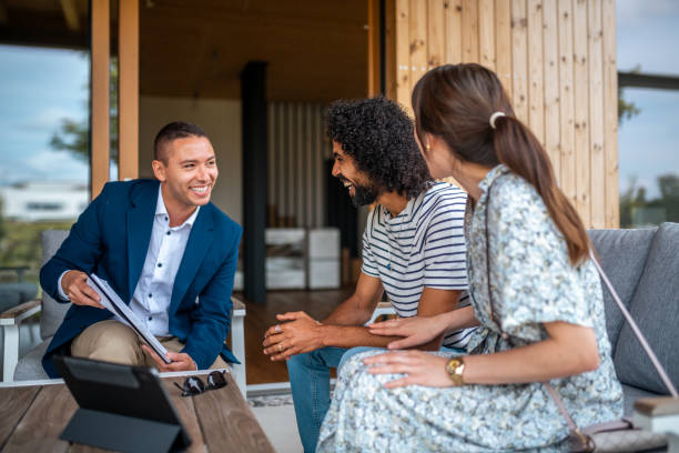 A professional Hispanic real estate agent discusses architectural plans with an engaged diverse couple, providing guidance on a modern patio setting.