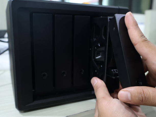 istock close up of someone's hand inserting a hard disk into a black Network Attached Storage 2205069449