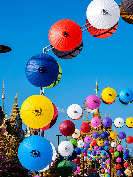 A vibrant display of colorful umbrellas hangs above the golden gates of Wat Phiphat Mongkhon in Thung Saliam, Sukhothai, Thailand. The umbrellas create a cheerful and welcoming atmosphere, contrasting beautifully with the ornate golden architecture of the temple entrance ,Left Side ViewA vibrant display of colorful umbrellas hangs above the golden gates of Wat Phiphat Mongkhon in Thung Saliam, Sukhothai, Thailand. The umbrellas create a cheerful and welcoming atmosphere, contrasting beautifully with the ornate golden architecture of the temple entrance