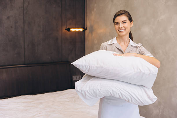 istock Smiling chambermaid holding two white pillows in hotel room 2205073006