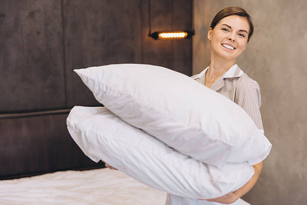 istock Smiling chambermaid holding two white pillows in hotel room 2205073078