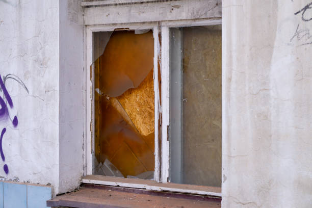 Shattered glass frames a view of a dilapidated interior filled with debris, revealing the neglected state of an abandoned building