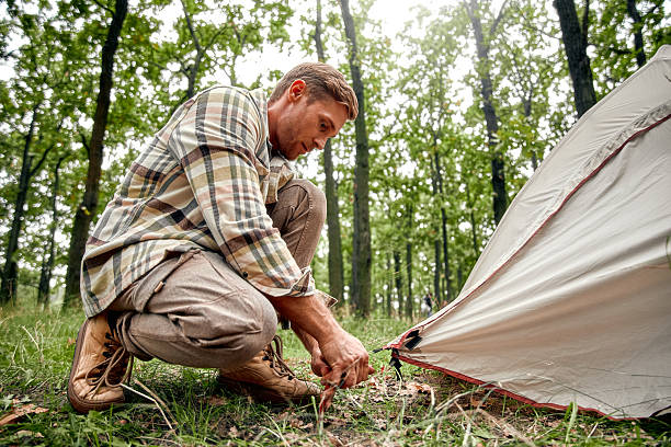 istock A man is diligently setting up a tent in a beautifully lush and vibrant forest campground 2205085005