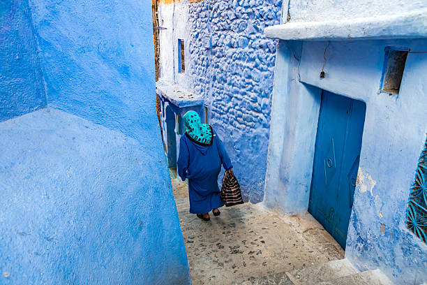 A woman walking on the steps of a street in the blue city of Chefchaouen, Morroco