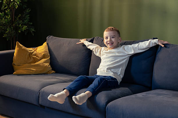 istock Happy child relaxing on sofa at home: spreading arms and smiling 2205087371