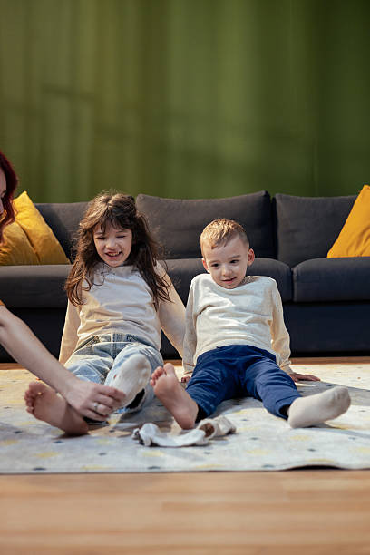 istock Mother putting socks on daughter while brother is sitting next to her on carpet 2205088405