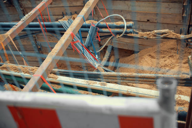 Protective ribbed plastic hoses for cables are placed and connected to distribution box, under rusty rebar, prepared for pouring concrete over them. Residential building under construction.