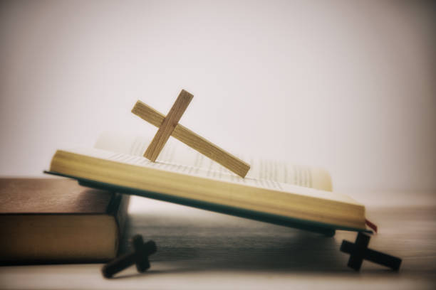 Old open Bible on a wooden table with several wooden crosses and isolated white background. Side view.