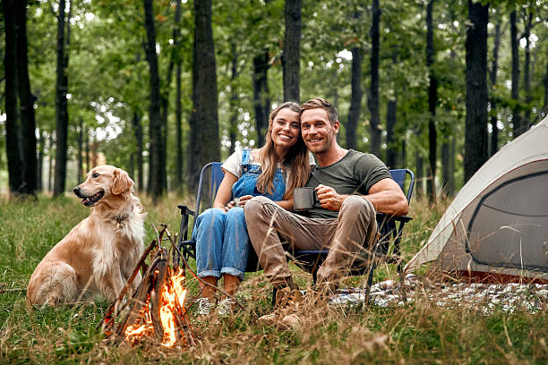 istock A couple enjoys camping by a warm fire with their dog in a serene forest setting 2205094497