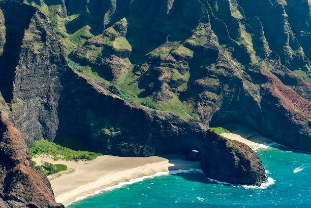 As photographed from an open-air helicopter off the Na Pali coast in Kauai is the Honopu Beach, made famous by the second King Kong movie.  A small boat can be seen approaching the main prominence formed by  an old volcanic flow.  It is shaped like a giant arm that appears to protect the beach.