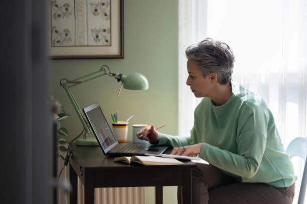 istock Happy middle aged woman sitting at table and using laptop in modern house 2205098030