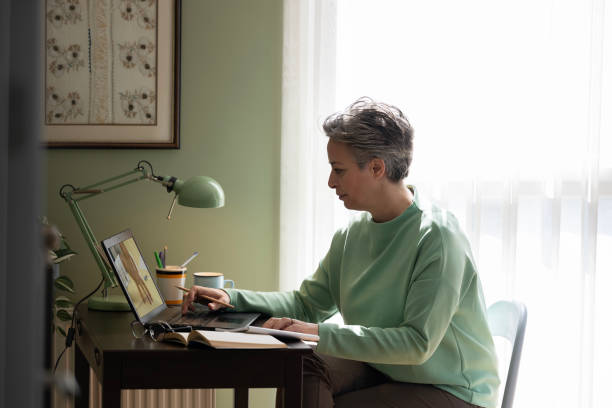 istock Happy middle aged woman sitting at table and using laptop in modern house 2205098031