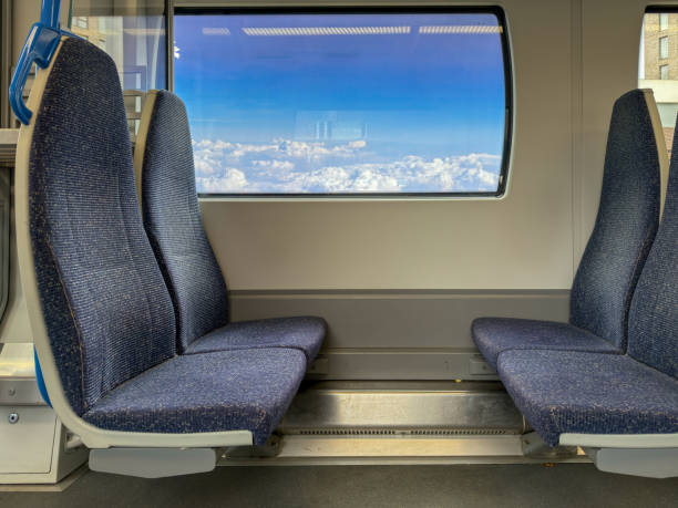A clean and modern train interior featuring empty seats and a large window with a bright blue sky view. The spacious and comfortable design highlights efficient public transportation and urban commuting. Ideal for concepts of travel, mobility, railway systems, and transportation infrastructure.