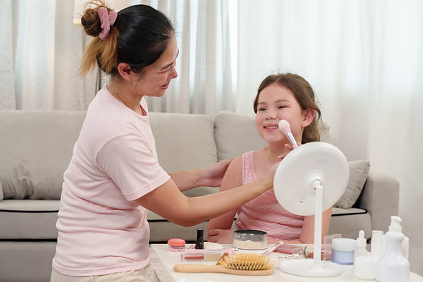 istock Asian mother and Caucasian daughter smiling while playfully applying blush on cheeks during fun makeup session. Skincare products and beauty tools neatly placed on table in cozy home atmosphere. 2205106080