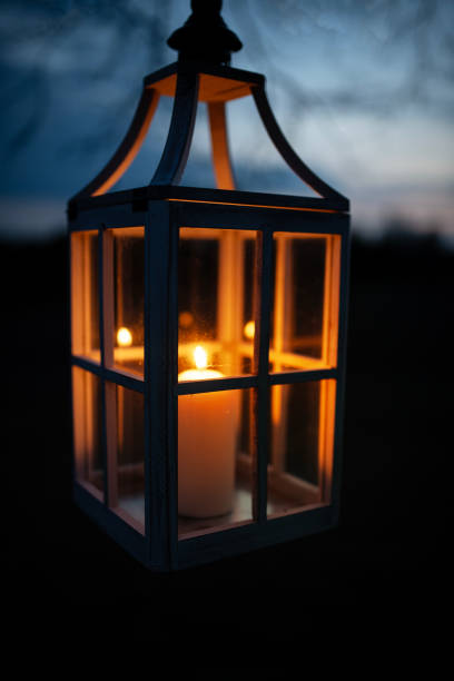 istock Glowing Lantern Hanging from a Tree Branch at Twilight Against a Dark Sky 2205106306