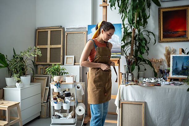 istock Cheerful woman painter tying apron getting ready for creative work. Female artist at art workshop 2205107239