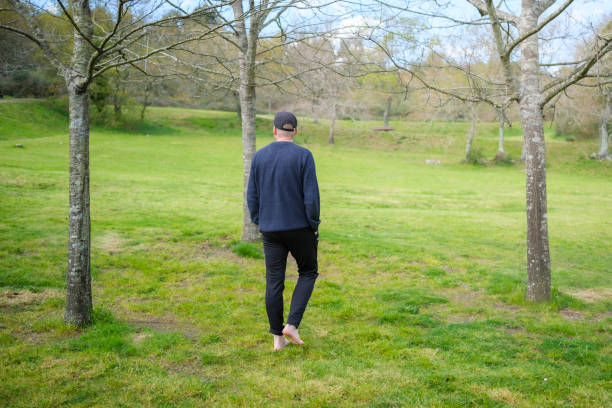 istock Man walking barefoot on grass in peaceful park setting 2205109691