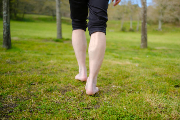 istock Man walking barefoot on grass in lush green park 2205109813