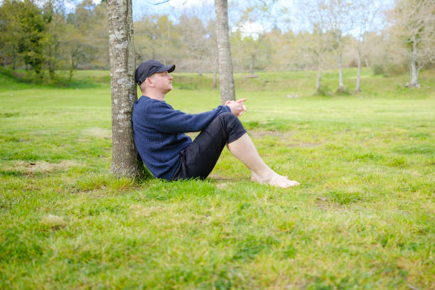Man enjoying peaceful moment in nature, sitting under tree in green meadow