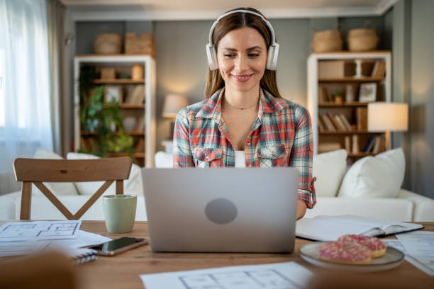 istock Architect working from home on a laptop wearing headphones and smiling 2205111614