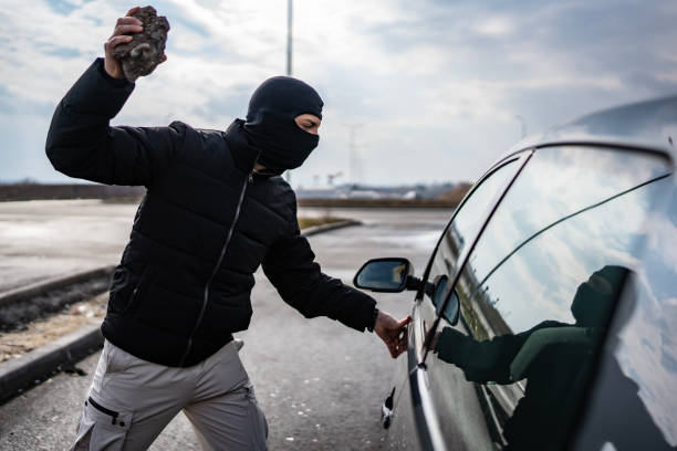 istock Masked Individual Holding a Rock Near a Parked Vehicle 2205113740