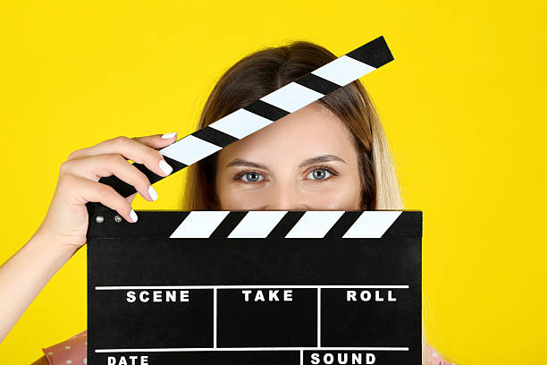 istock Young woman with blank clapper board on yellow background 2205117181