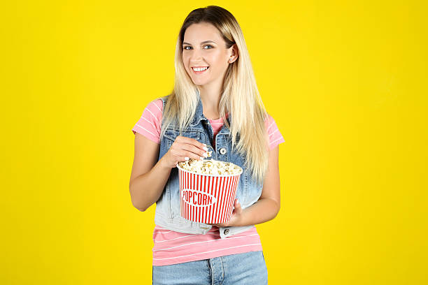 istock Young woman holding bucket with popcorn on yellow background 2205117218