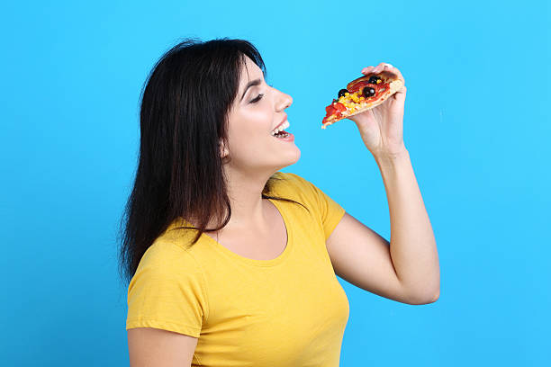 Young woman eating pizza on blue background