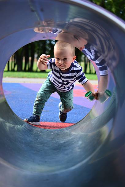 istock Toddler boy playfully looking through crawling tunnel in playground. Kid is getting into crawling tunnel in playground. Round frame boy portrait outside. 2205121670