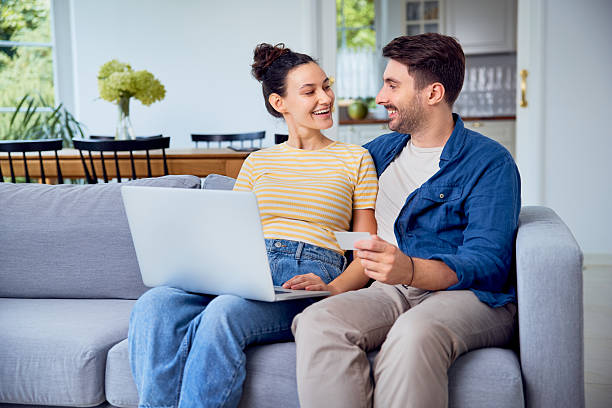istock Smiling young couple shopping online using laptop sitting on a sofa at home 2205123274