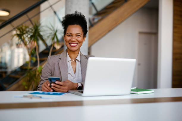 istock Smiling businesswoman using smartphone and laptop in modern office 2205123773