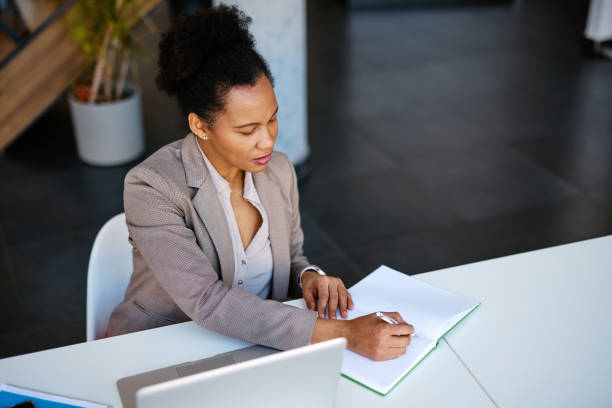 istock Focused businesswoman writing notes in notebook at modern office desk 2205123796