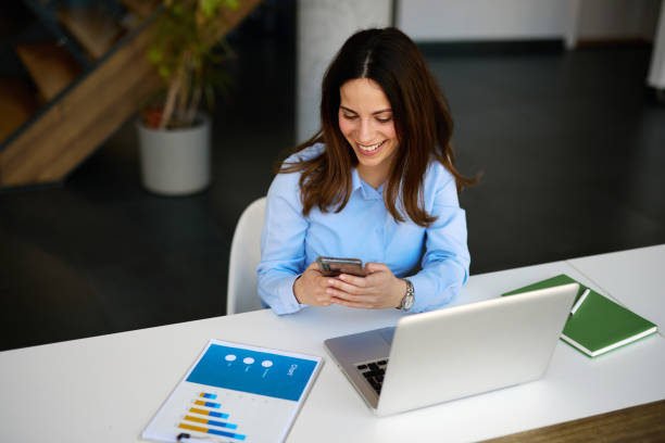 istock Young businesswoman using smartphone and smiling in modern office 2205123811