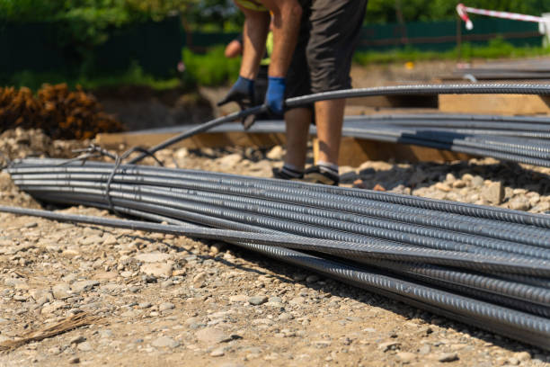istock Construction worker bending steel reinforcement bars for foundation work, preparing the site for pouring concrete, ensuring structural integrity and longevity of the building 2205124234