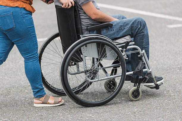 istock Assistant helping a man with reduced mobility in a wheelchair to move 2205124729