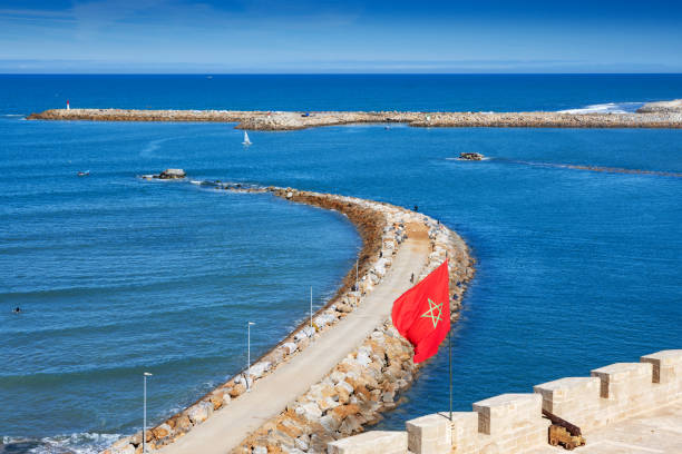 Panoramic view of a sandy beach and ocean waves, featuring a fortress wall and bright sky.