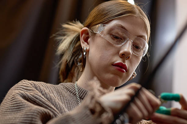 Close-up of a focused woman wearing safety glasses and working in a workshop environment, concentrating on a task with precision and attention
