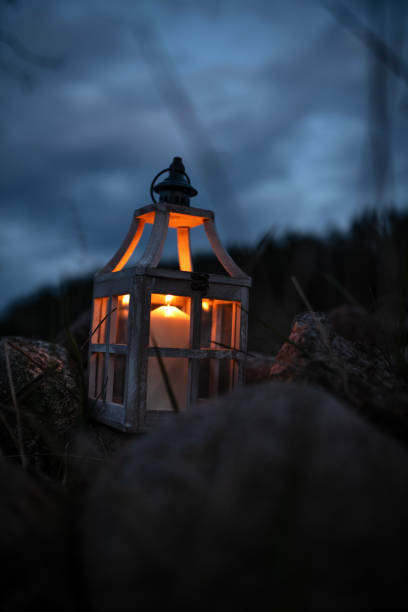 istock Close-up of a Glowing Candle in a Rustic Lantern Among Rocks at Night 2205128479
