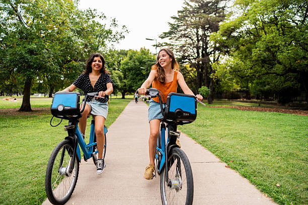 istock Sisters riding bikes in a public park 2205134009