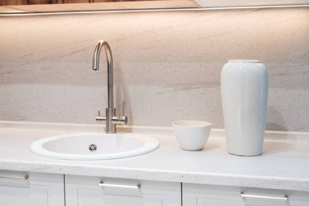 istock White sink with silver faucet in modern kitchen interior. White bowl and white vase on countertop. 2205134191