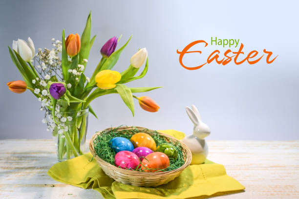 istock Colorful Easter eggs in a basket, spring bouquet with tulips and a small bunny, text Happy Easter, light blue gray background, copy space, selected focus 2205134721