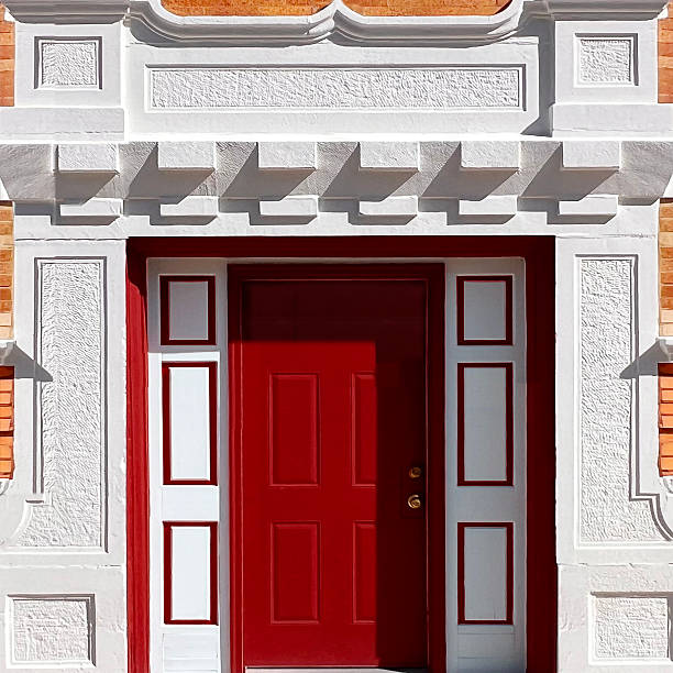 A striking red double door contrasted beautifully against a white architectural facade, showcasing classic design elements and symmetry. Perfect representation of elegance and historical urban charm.