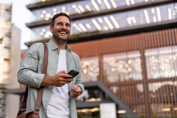 istock Smiling businessman using smartphone in front of modern office building 2205138566