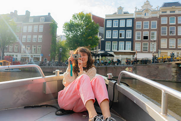 Woman photographing with camera during boat ride exploring canals in  Amsterdam on sunny day